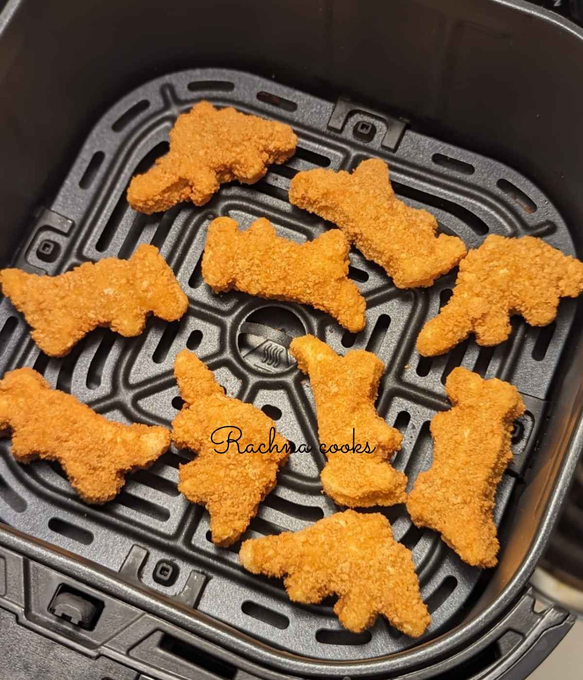 Frozen dino nuggets placed in air fryer basket for air frying.