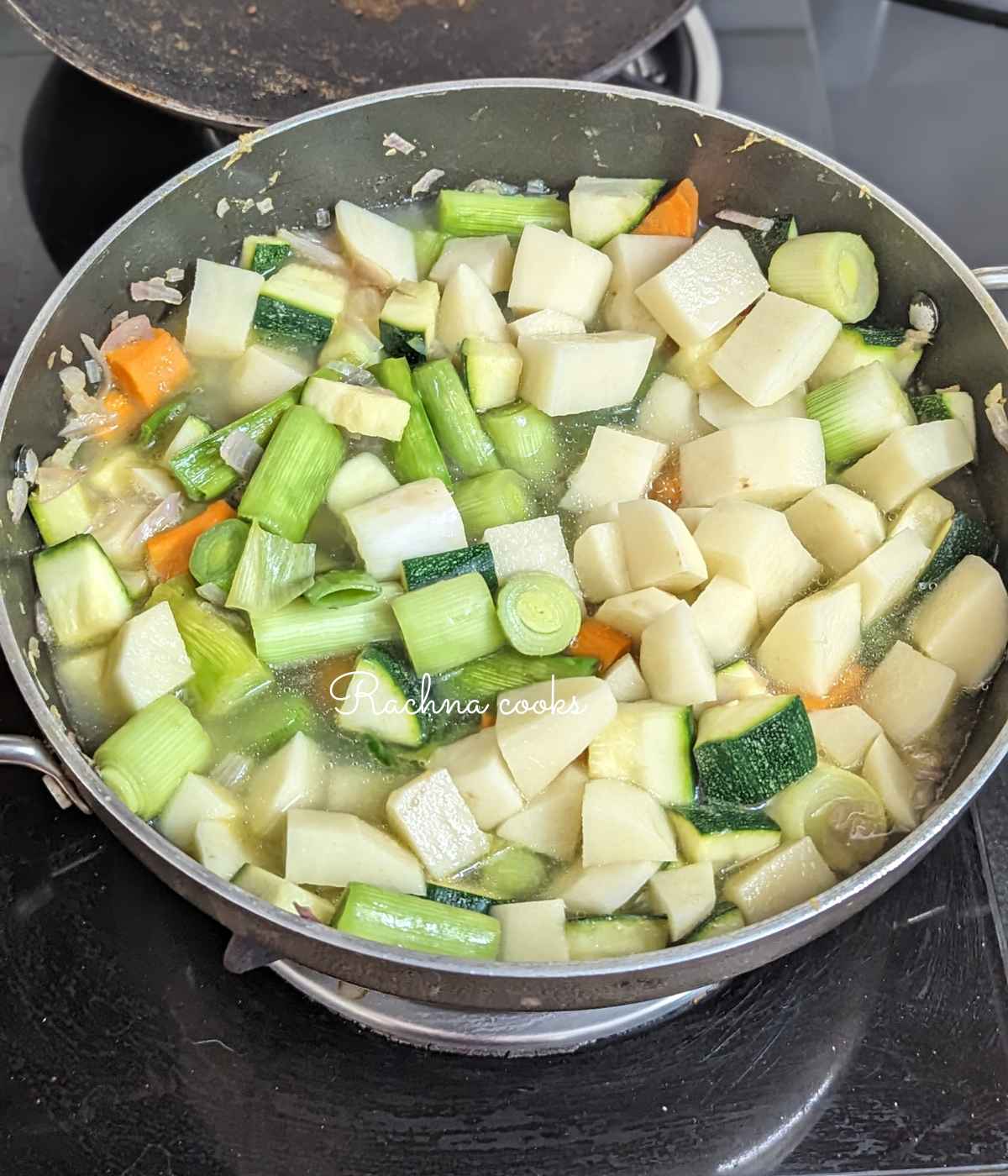 Potatoes, leeks, zucchini, carrot, cauliflower, onion and garlic with stock in a pan.