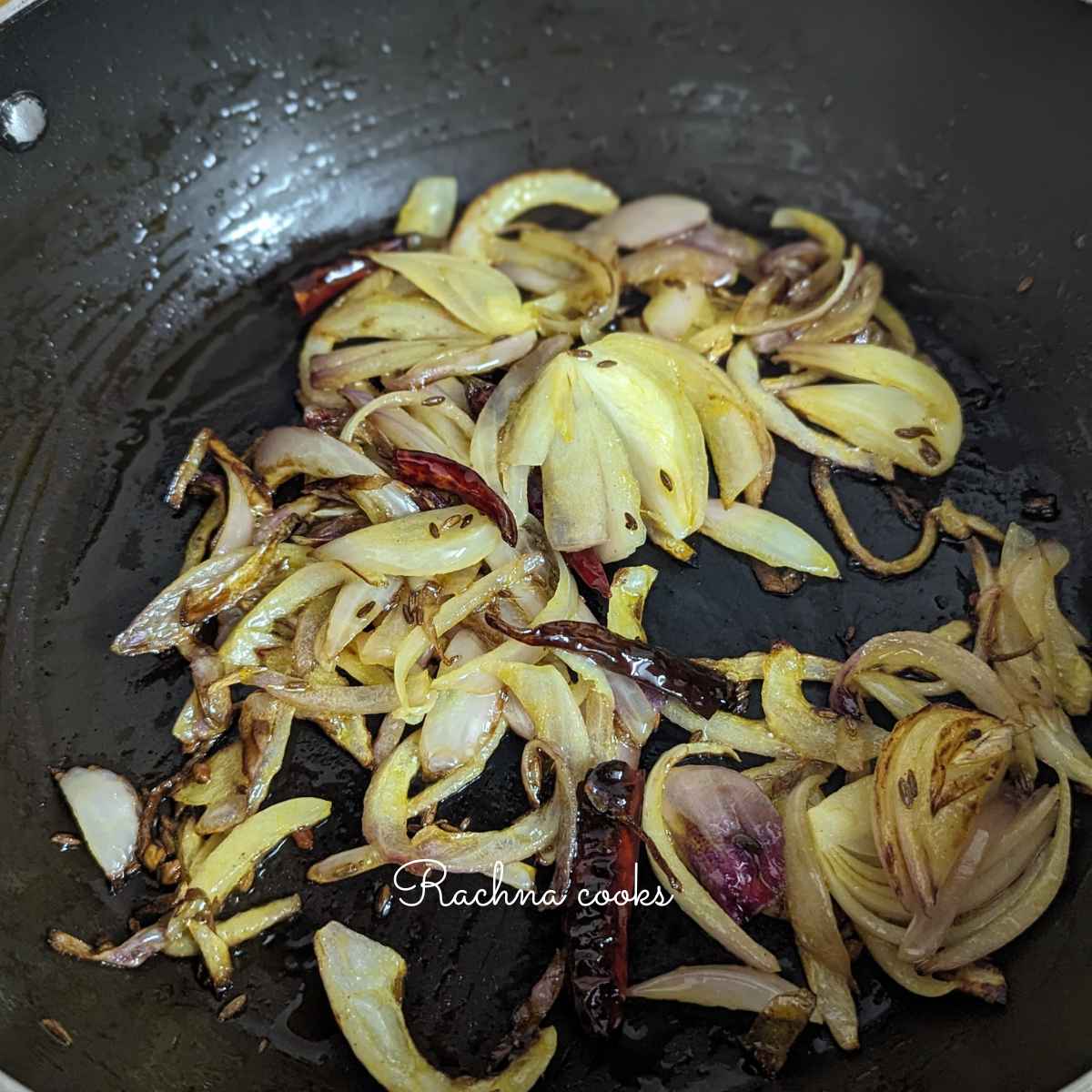 Slightly browned sliced onion with dry red chillies and cumin seeds in a pan.