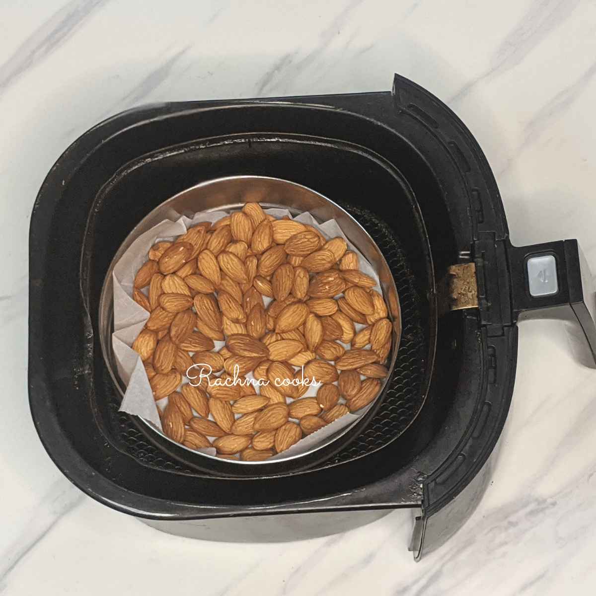 Almonds in a cake tin lined with parchment paper in air fryer basket.