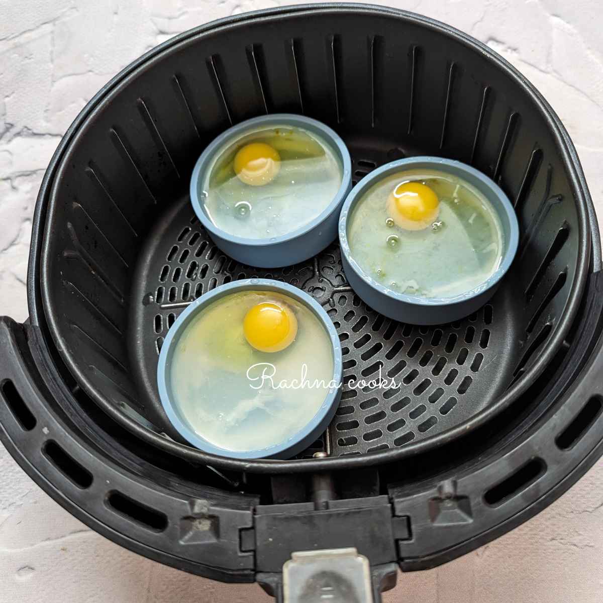 Cracked egg in silicone molds topped with hot water in air fryer basket.