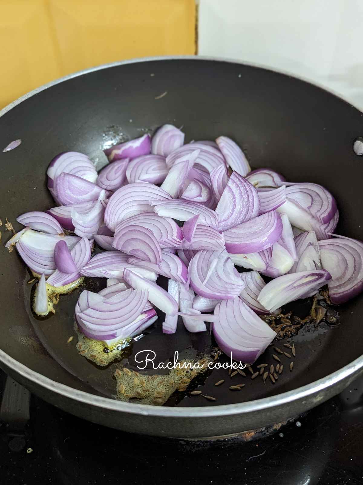 Sliced onion added to a pan with cumin seeds and oil.