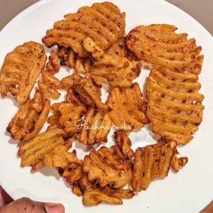 Frozen waffle fries after cooking in air fryer served in a white plate.