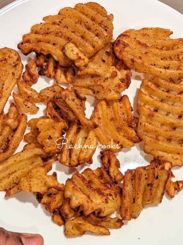 Frozen waffle fries after cooking in air fryer served in a white plate.
