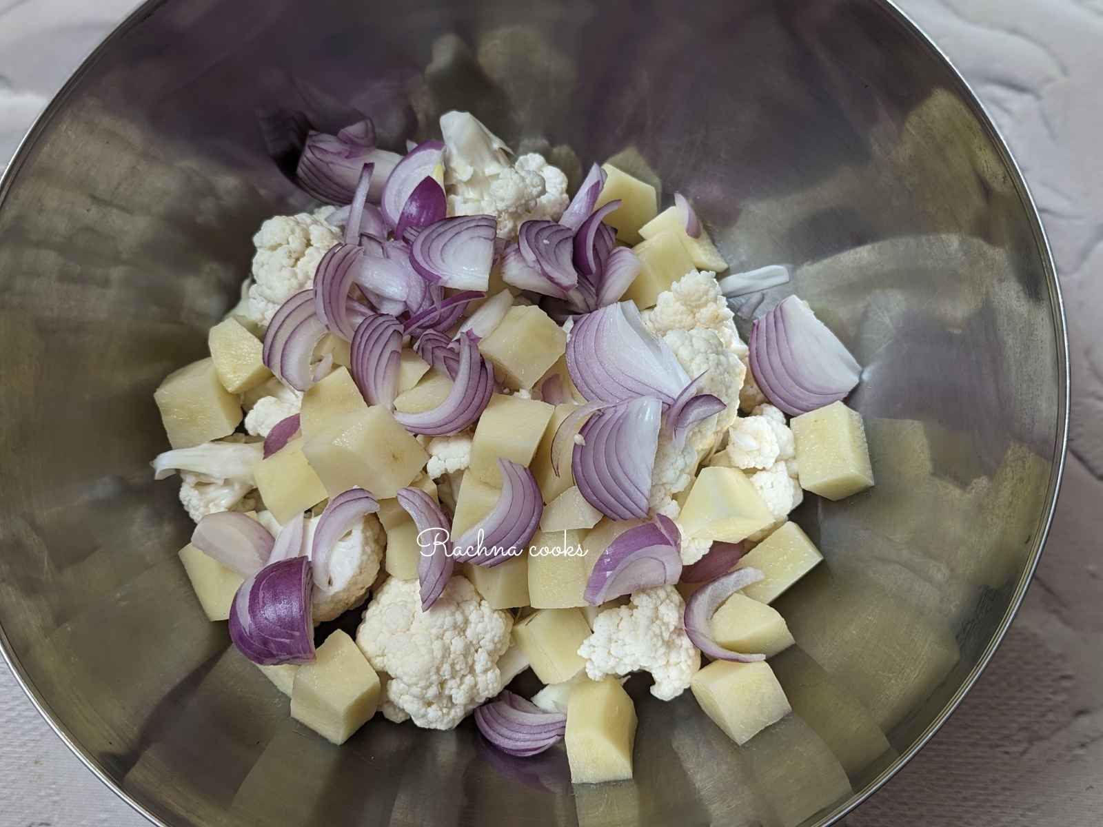 Cauliflower florets, peeled and cubed potatoes and sliced onion in a bowl