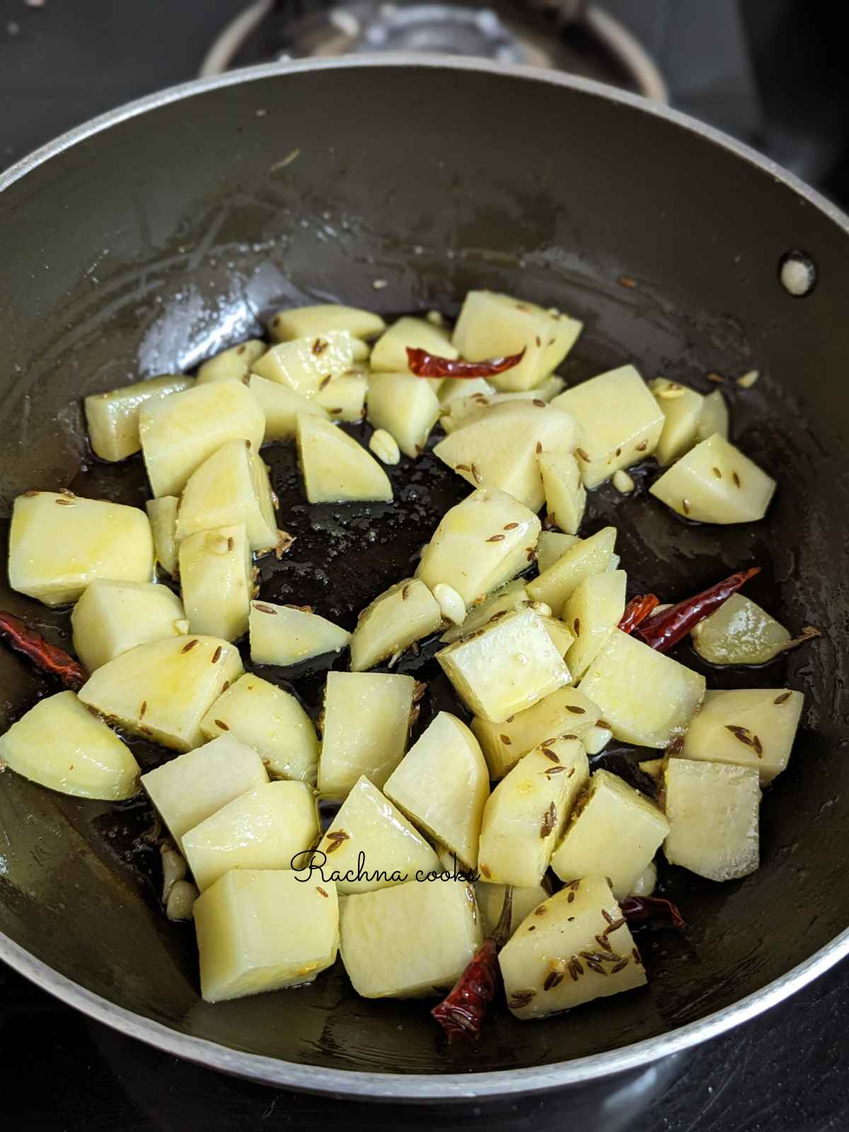 Chopped and cubed potatoes added to oil, cumin seeds and dry red chillies.