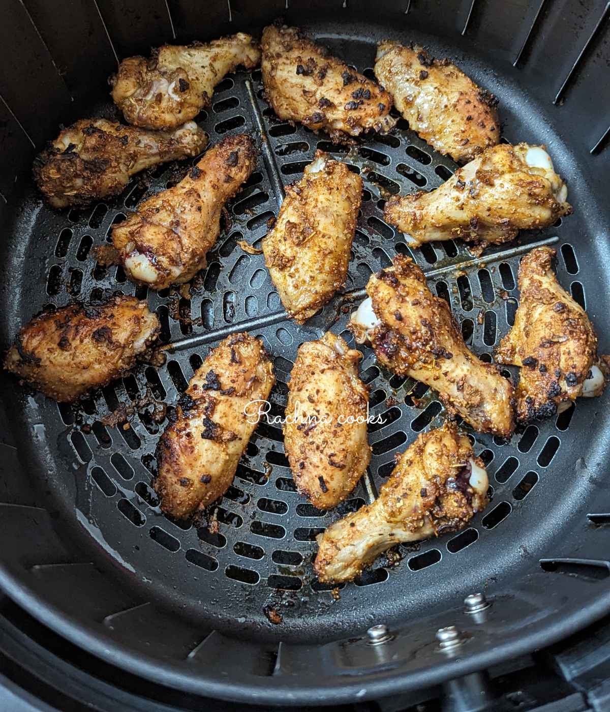 Jerk chicken wings after air frying in air fryer basket.