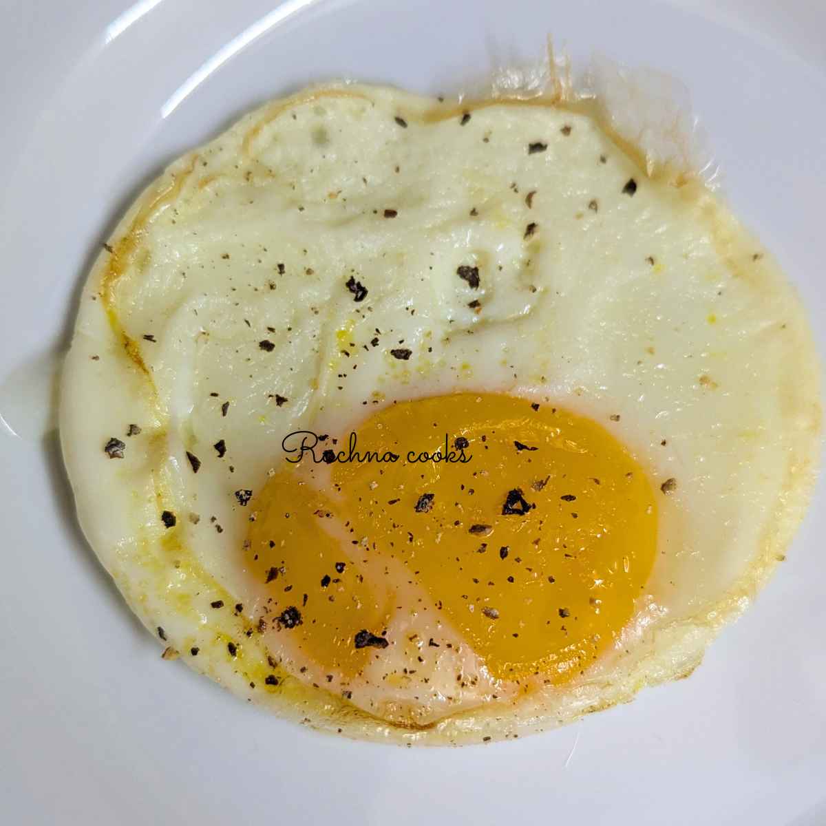 Delicious fried egg with salt and pepper on a white plate.