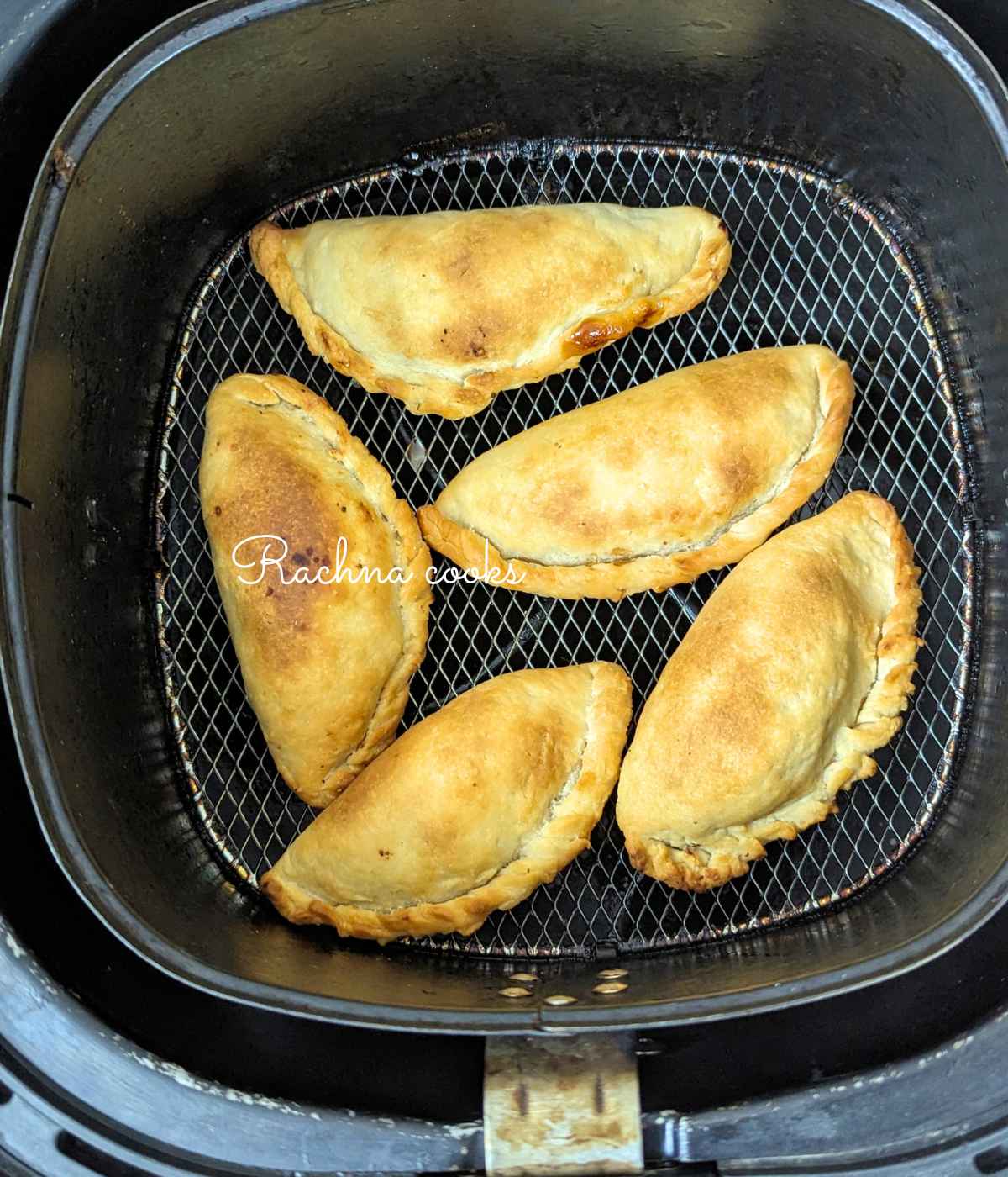 5 browned gujiyas after air frying in air fryer basket.
