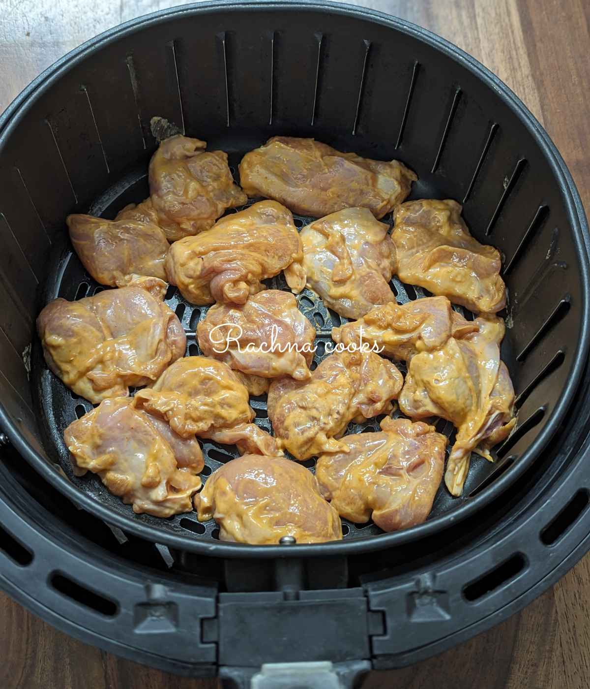 Marinated chicken bites laid in air fryer basket.