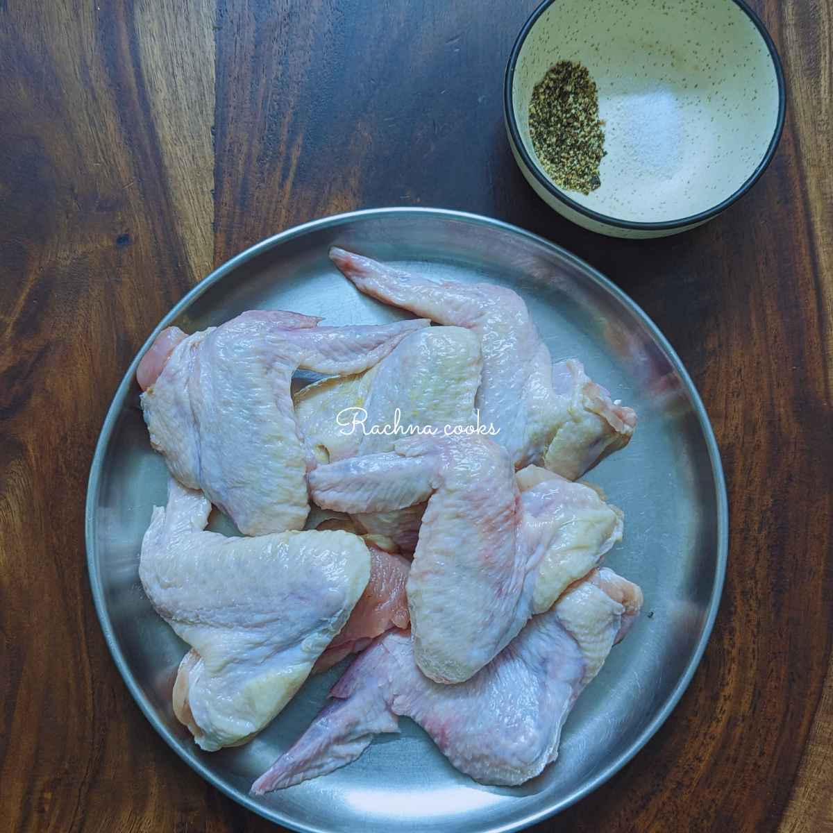Chicken wings on a plate with salt and pepper in a bowl.