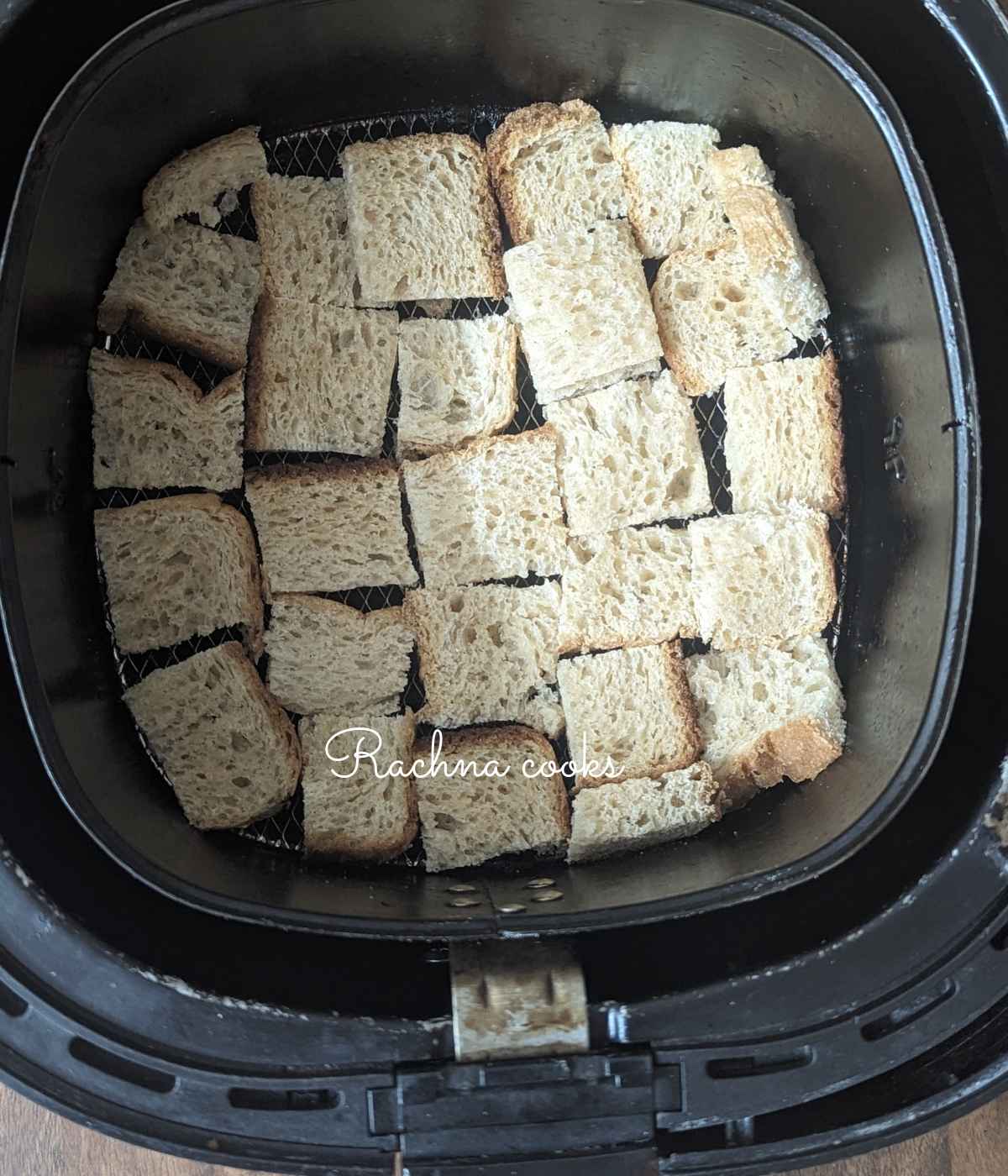 Bread cubes laid in air fryer basket for air frying.