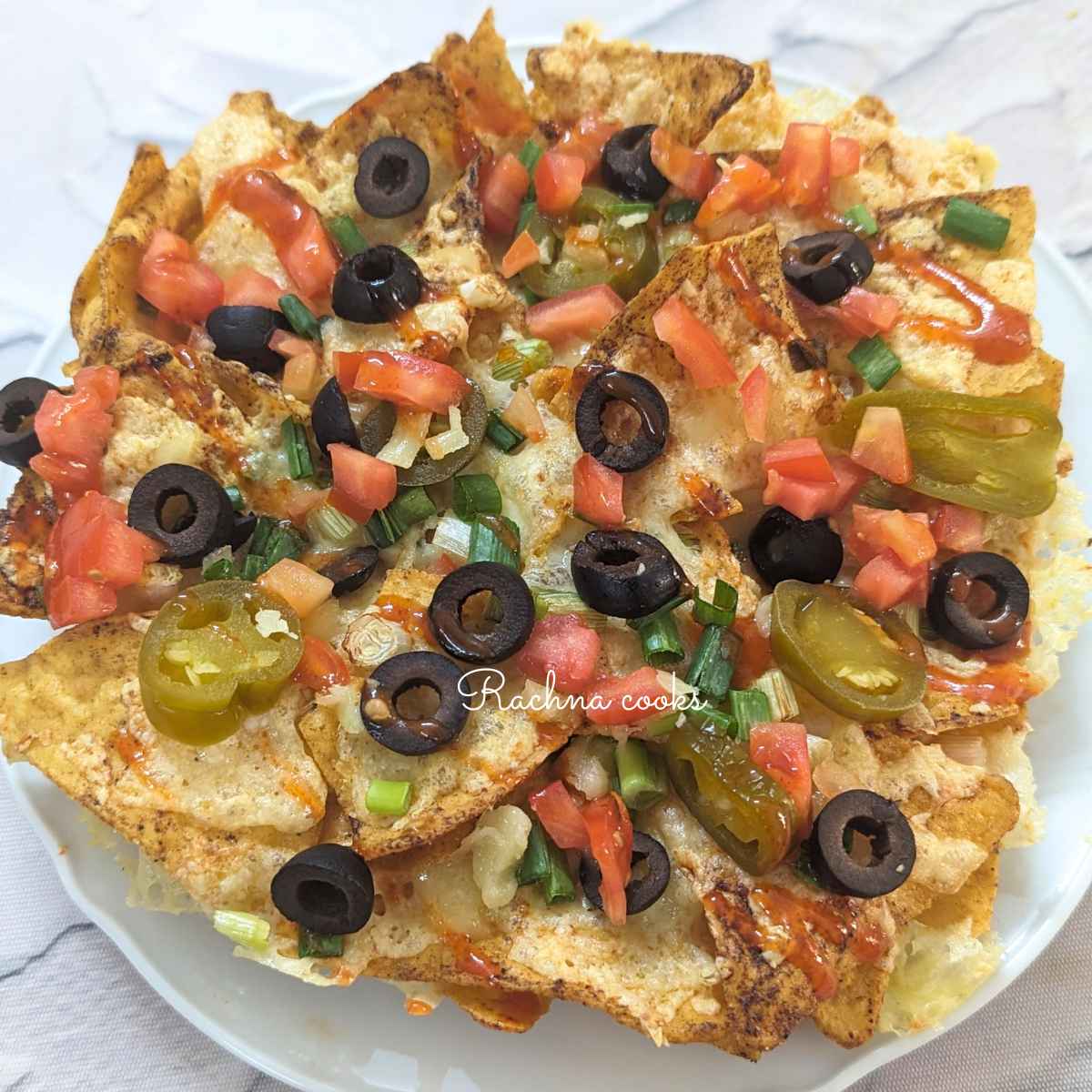 Loaded nachos with veggies and cheese served on a white plate.