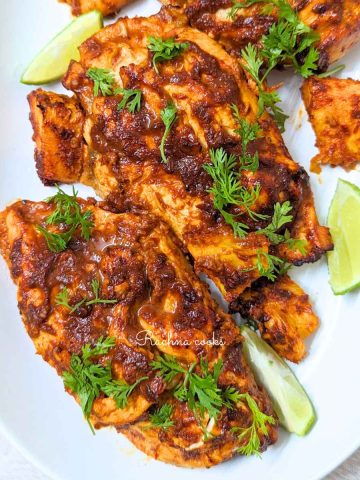 Chicken al pastor served on a white plate with lemon wedges and cilantro
