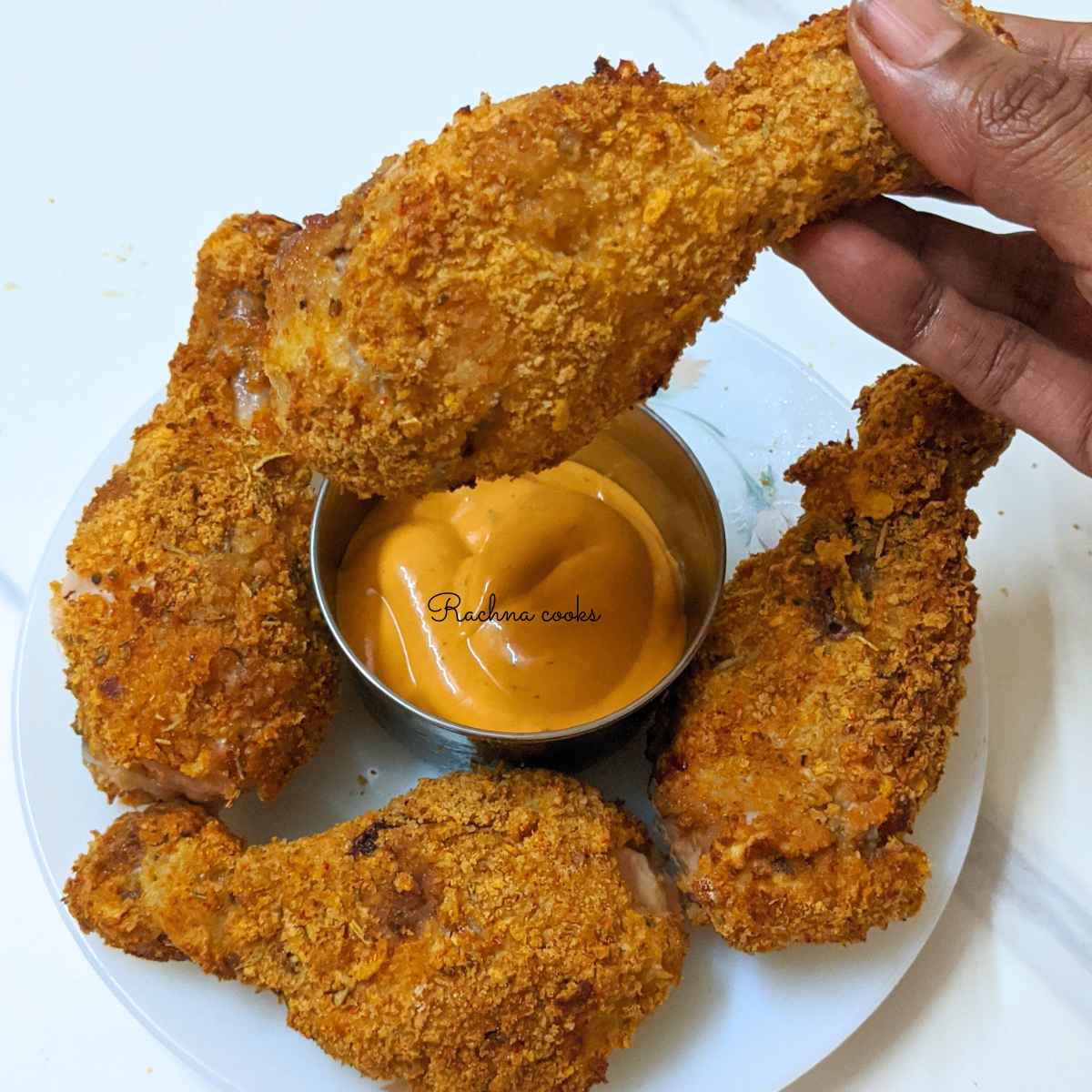 1 fried chicken drumstick held up in hand and 3 others in plate along with dip.