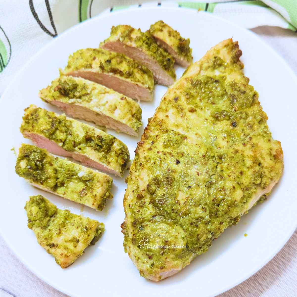 Air fried pesto chicken breasts served on a white plate. One breast is whole,the other is sliced.