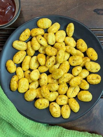 Air fried gnocchi on plate served with ketchup on the side.