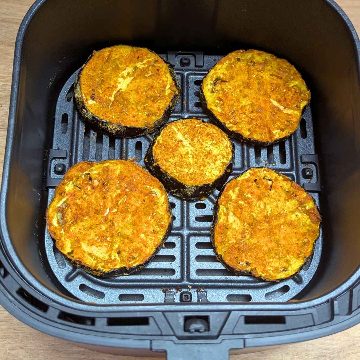 Seasoned eggplant slices after air frying in air fryer basket