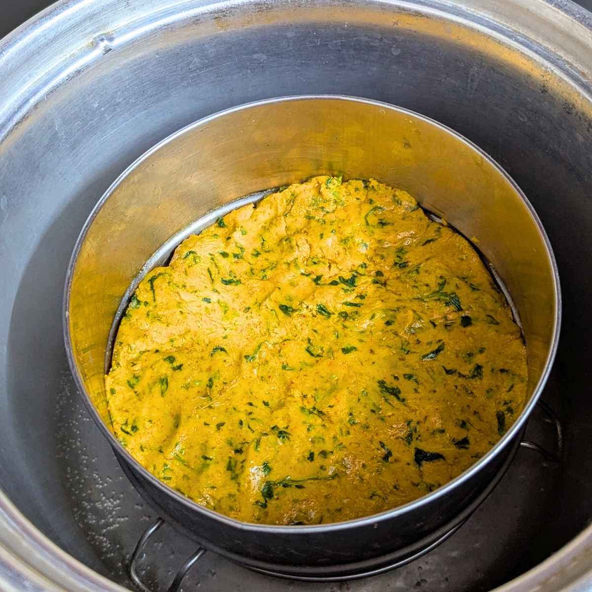 Kothimbir vadi dough being steamed in a cake tin.