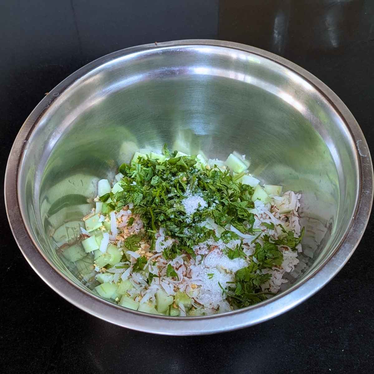 Cucumber with crushed peanuts, grated coconut, chopped cilantro and green chilli, salt, sugar and lemon juice in a bowl.