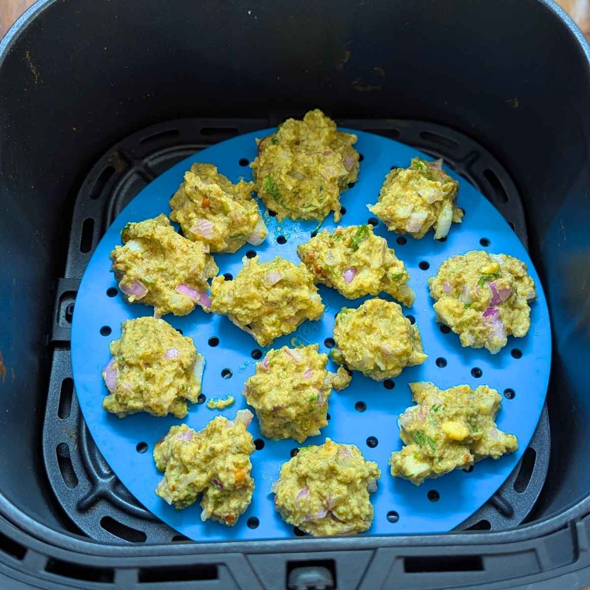 Moong dal pakode laid in air fryer basket for air frying.