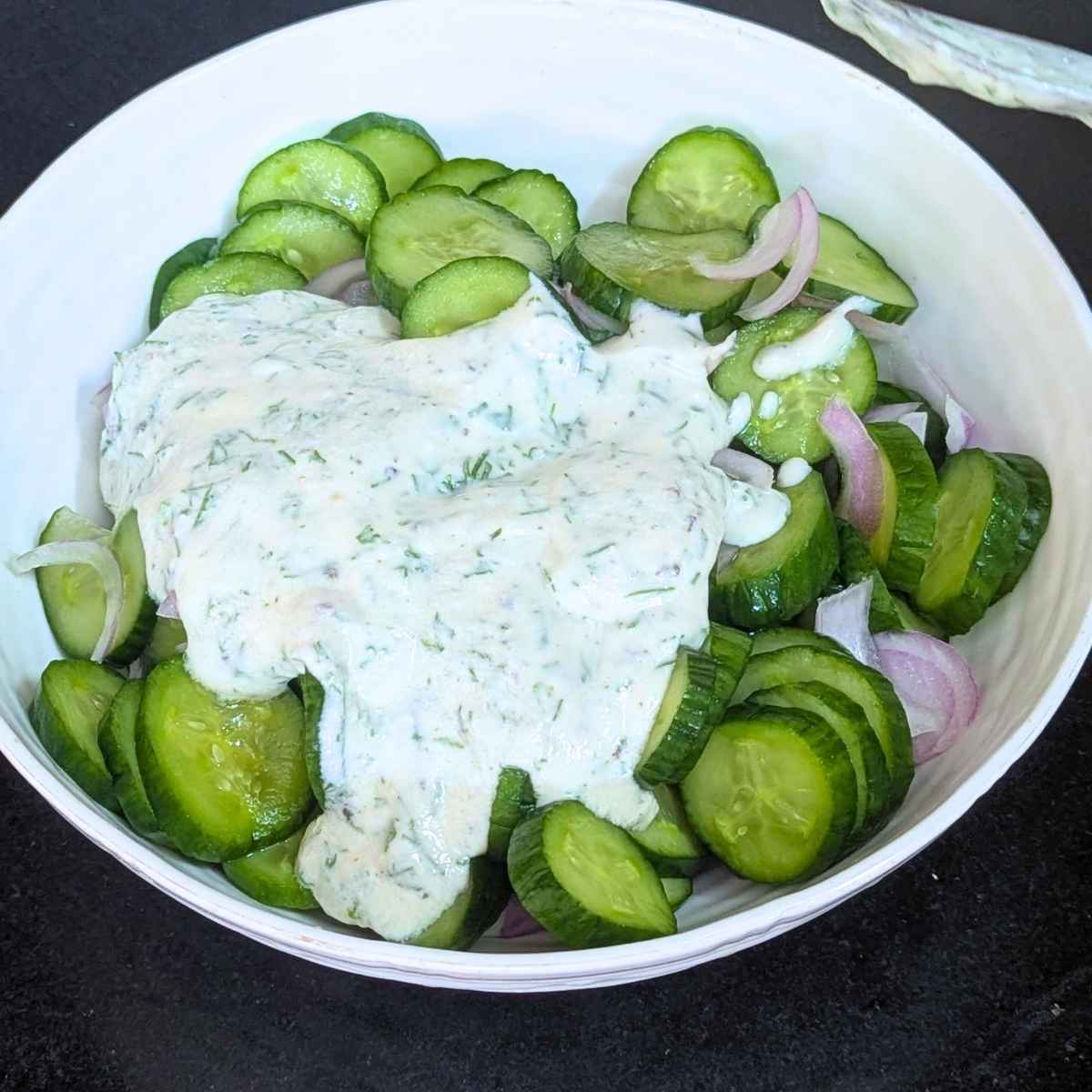 Creamy dressing poured on top of sliced cucumber and onion.