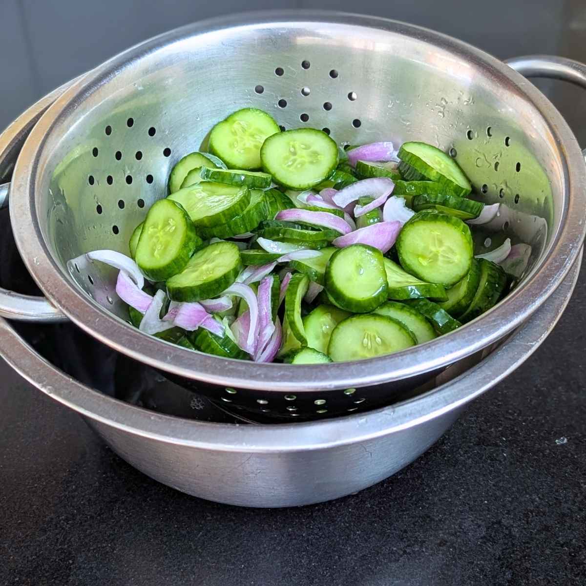 Cucumber and onion being drained in a colander after salting.