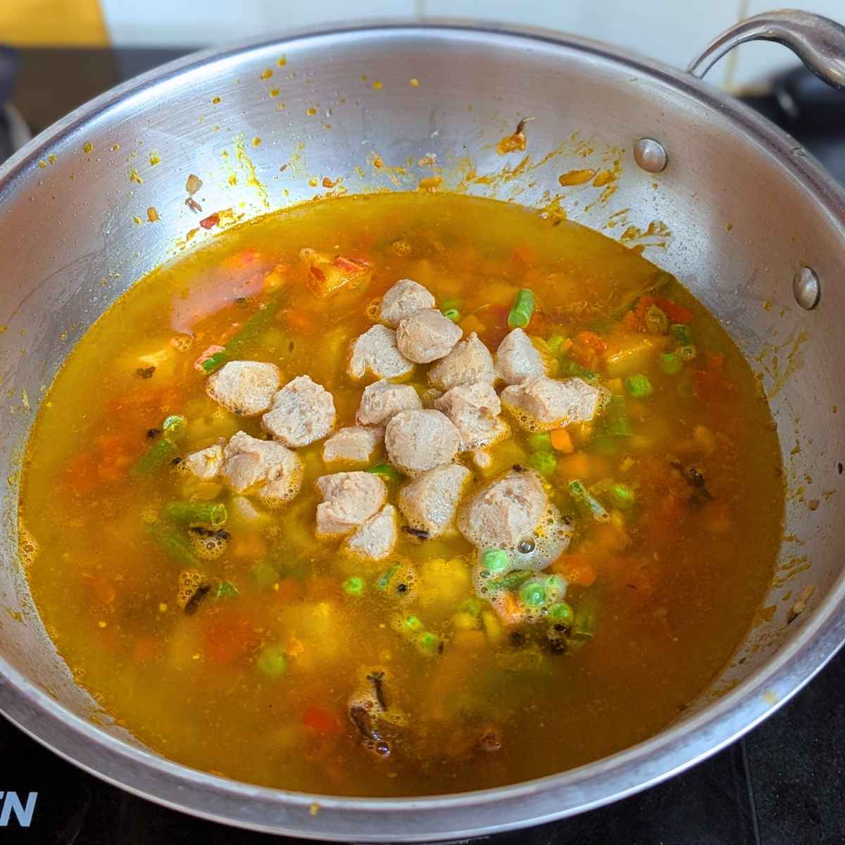 Boiled and drained soy chunks along with water and veggies added to the pan.