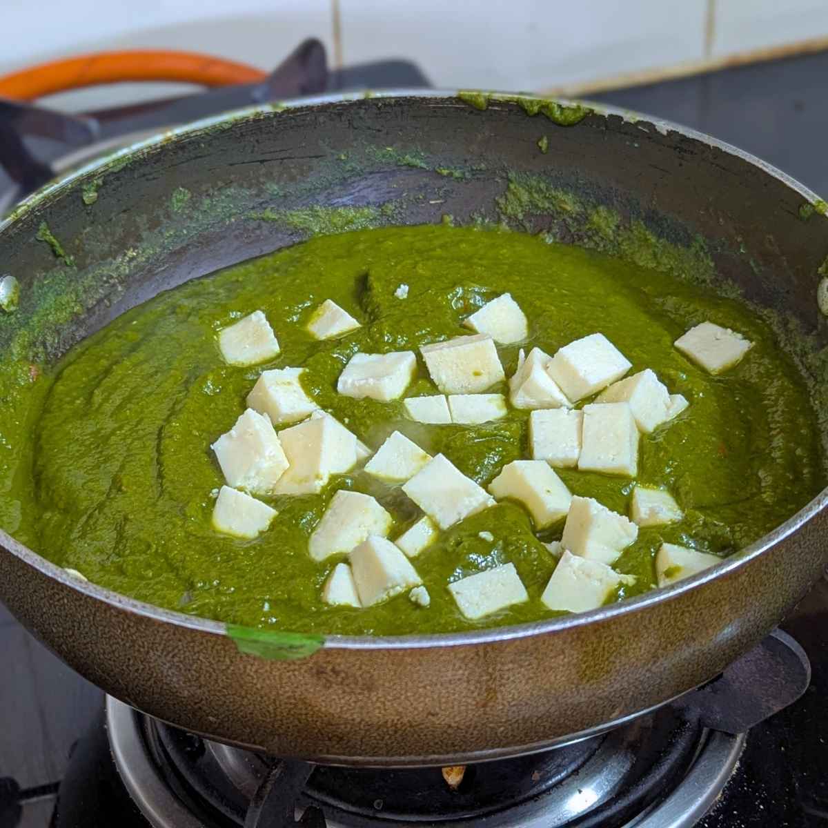 Spinach curry with paneer cubes in a pan.