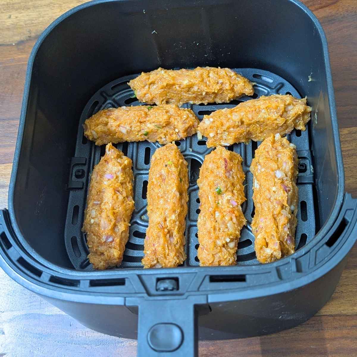 Chicken seekh logs kept in air fryer basket before air frying.