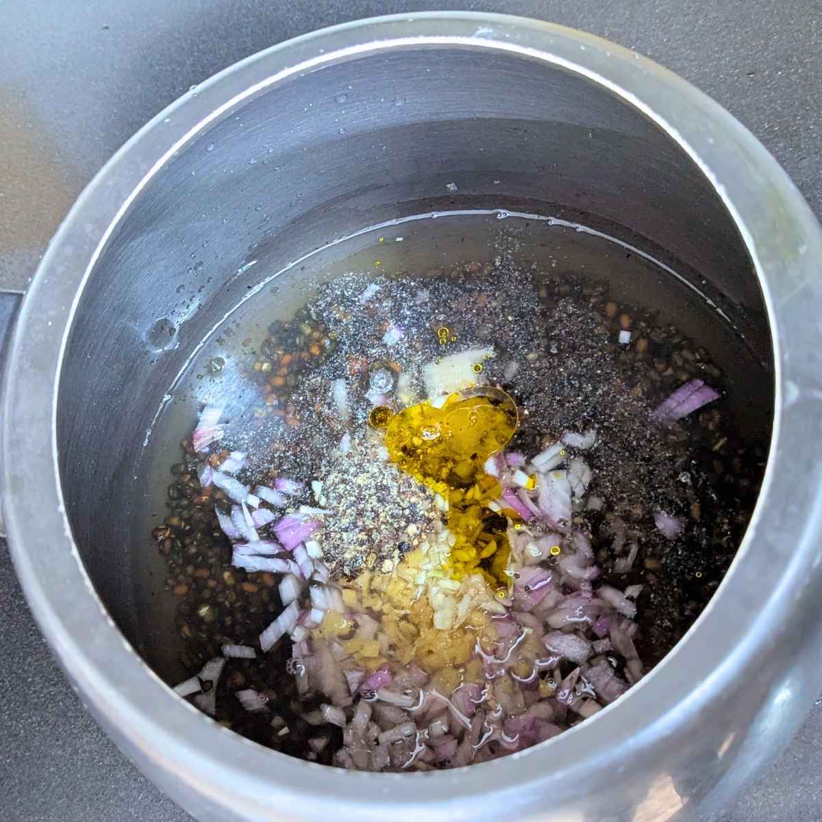 Chopped onion, ginger, garlic, salt, pepper, oil and heeng along with tomatoes added to soaked and washed black lentils in pressure cooker
