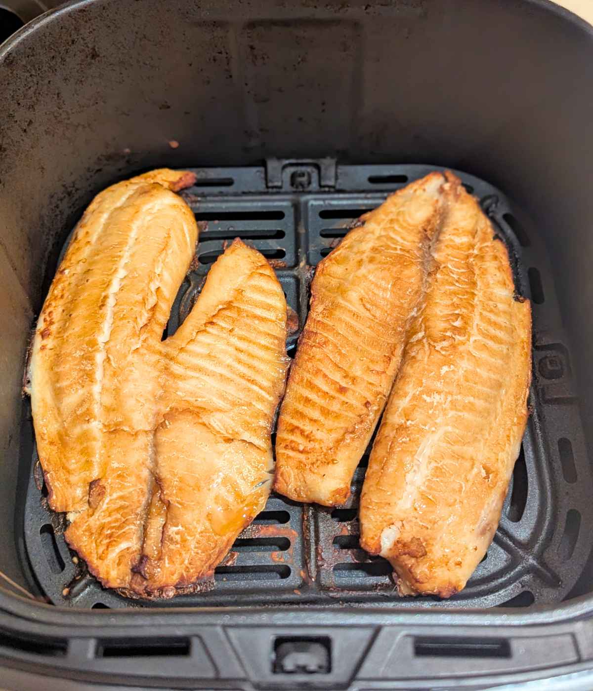 Tilapia fillets brushed with teriyaki sauce and after air frying in air fryer basket