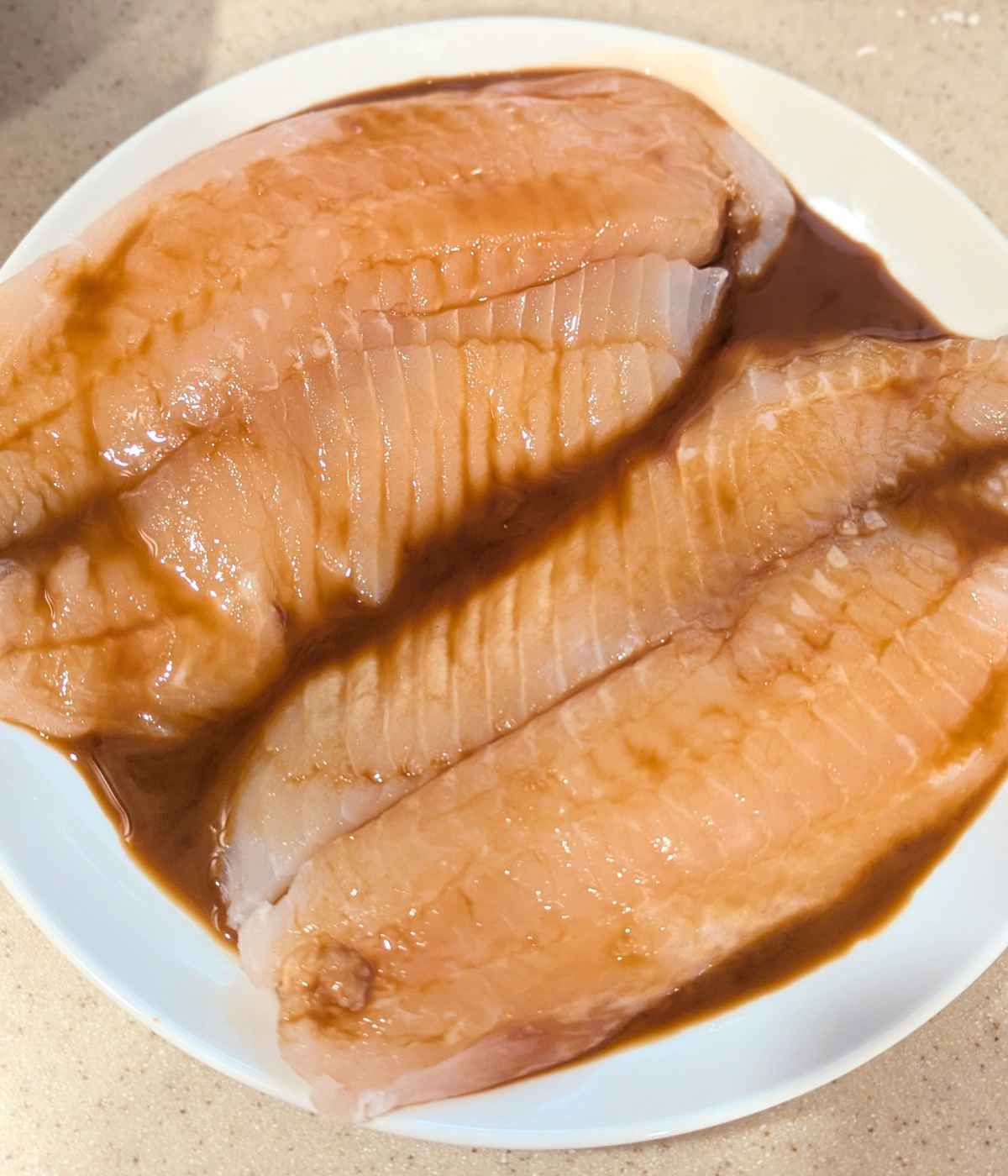 Tilapia fillets marinated in teriyaki sauce and placed on a white plate.