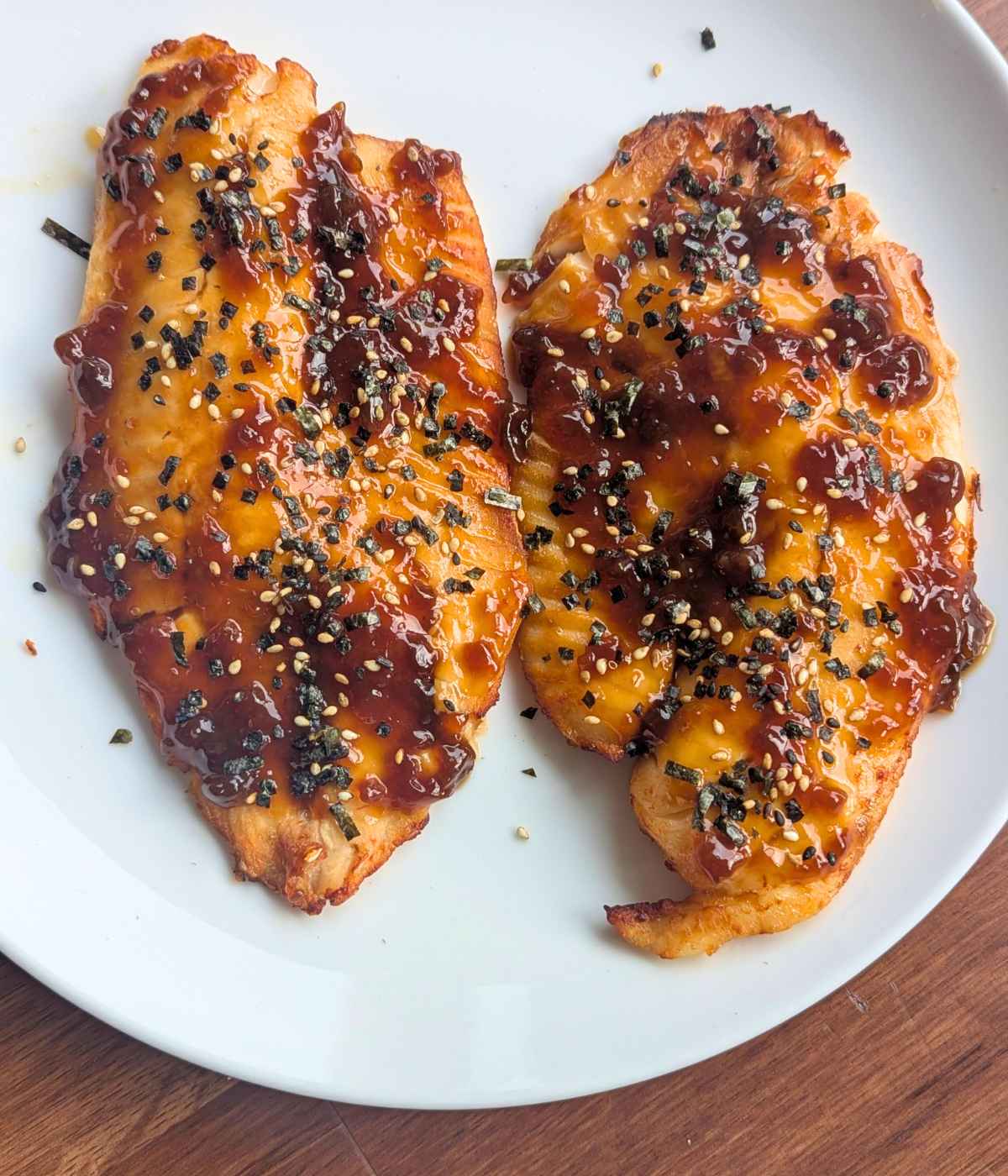 Teriyaki tilapia fillets garnished with furikake on a white plate.