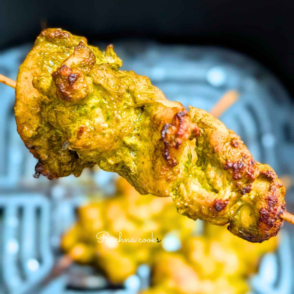One skewer of hariyali chicken tikka with slight char held up