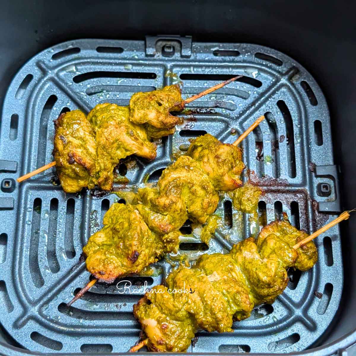 3 skewers of hariyali chicken tikka in air fryer basket after air frying