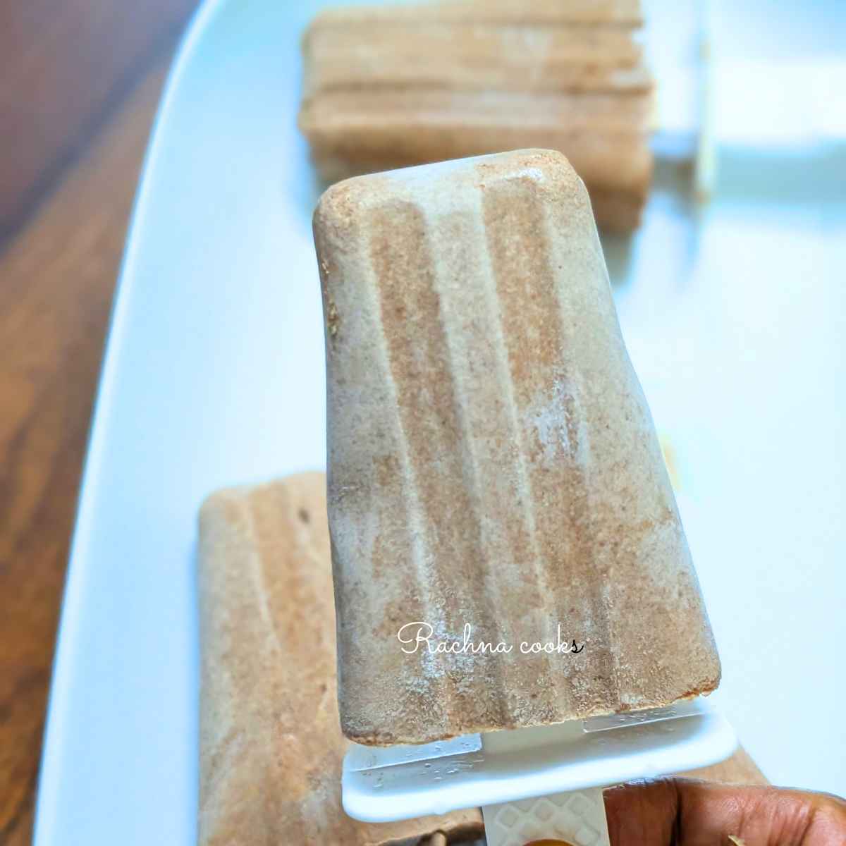 One chocolate yogurt popsicle held in hand against a white plate