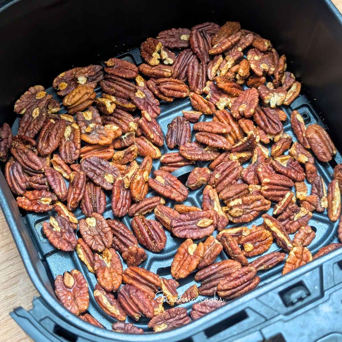 Golden pecans after roasting in air fryer visible in air fryer basket.