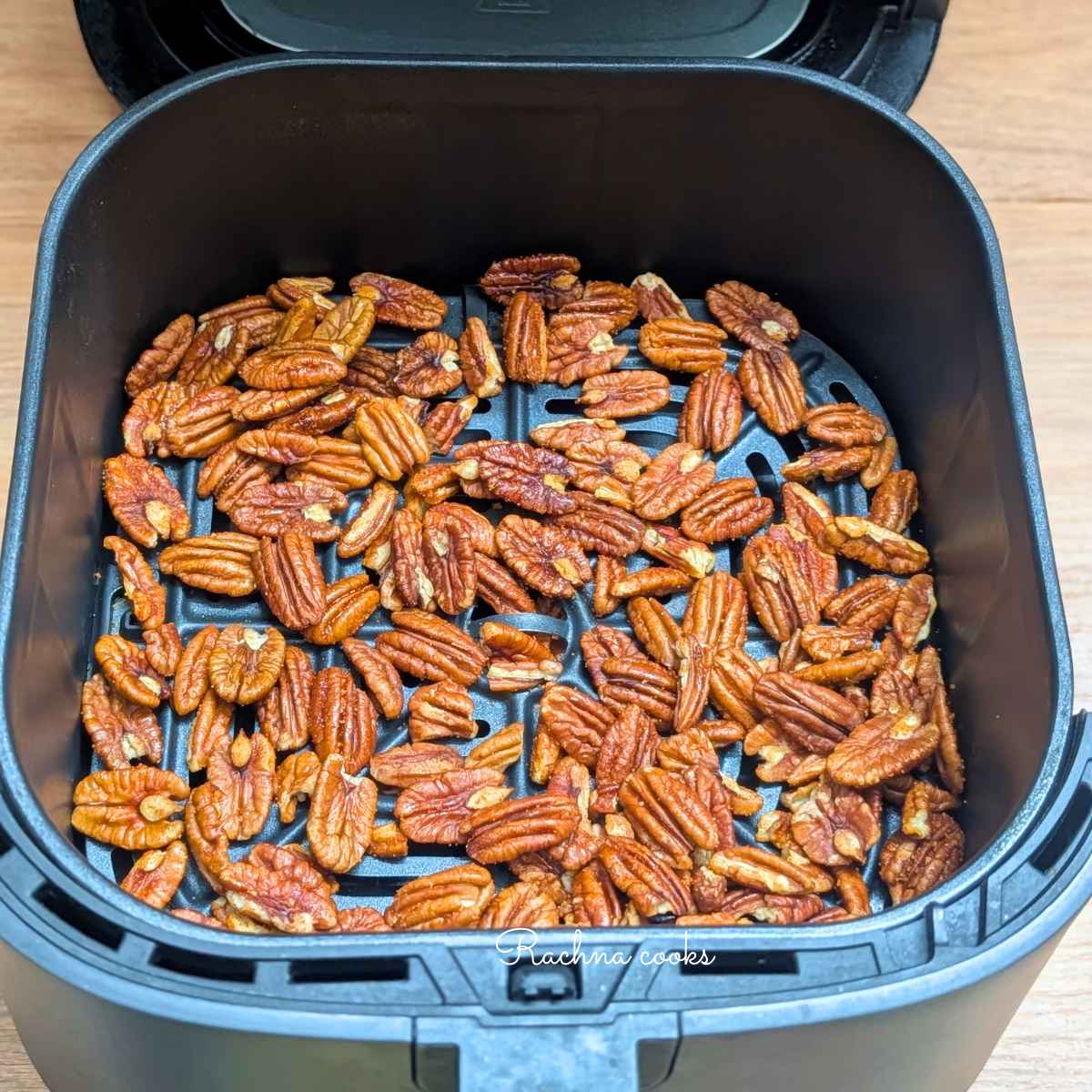 Raw pecans after adding seasonings being placed in air fryer basket for air frying.