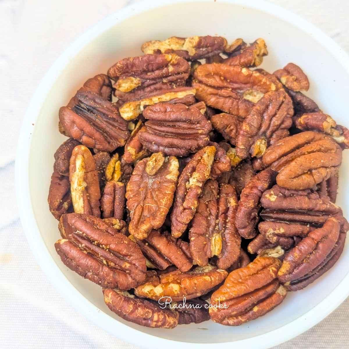 close up of golden brown toasted pecans after air frying and placing in white bowl