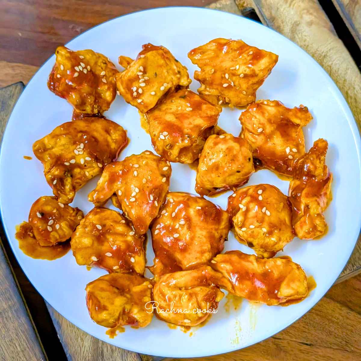 Glossy gochujang chicken bites served on a white plate with a garnish of sesame seeds.