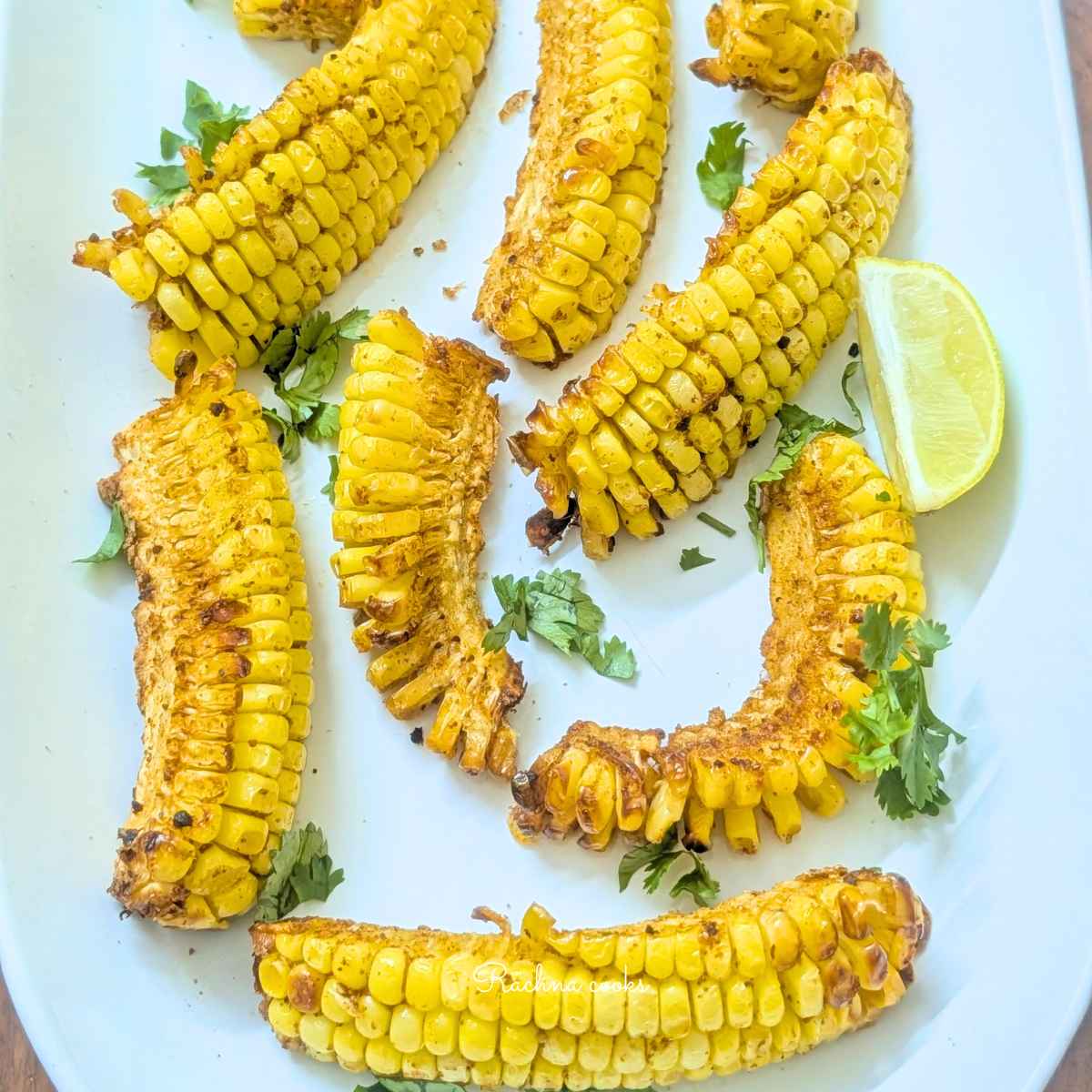 Golden brown corn ribs after air frying on a white plate garnished with cilantro and lemon wedges