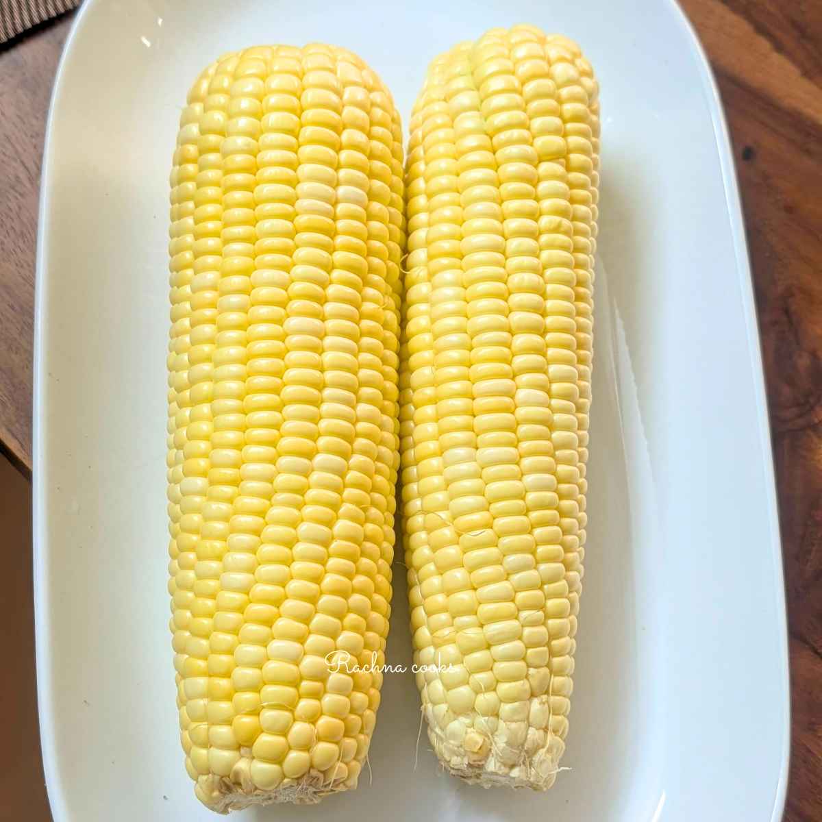 Two corn on the cobs on a plate after dehusking and removing the silks