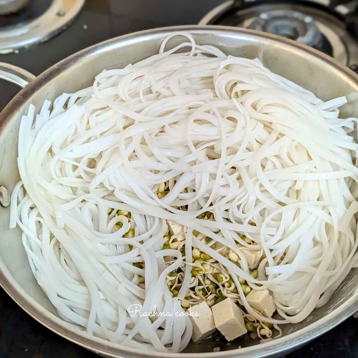 Noodles, bean sprouts and tofu visible in a large wok