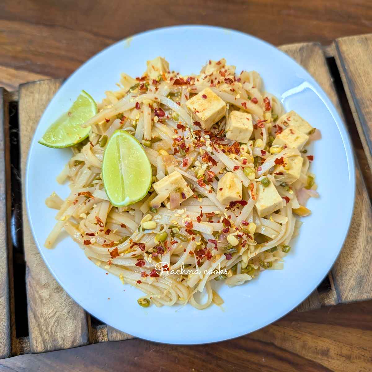 Pad thai noodles garnished with lemon slices and chili flakes on a white plate